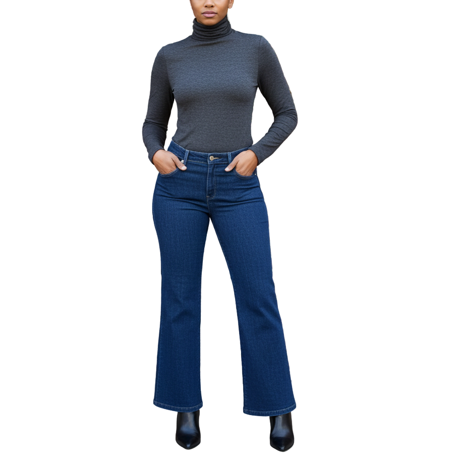 Woman wearing a gray turtleneck and blue jeans standing in front of a brick wall with greenery.