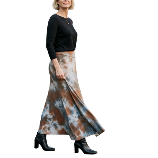 Woman wearing a black top and tie-dye skirt standing on a tree-lined street.