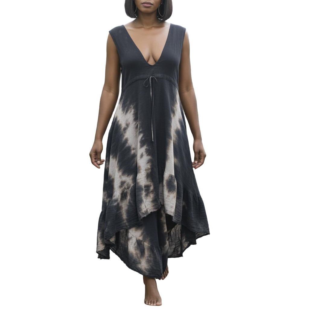 Woman in a black tie-dye dress walking through a greenhouse filled with plants.