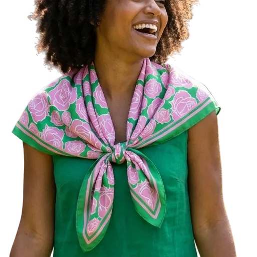 Woman in a green dress with a pink floral scarf standing in a garden.