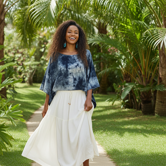 Woman in a blue tie-dye top and white skirt standing in a lush garden.