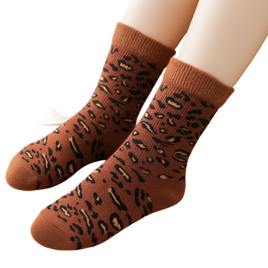 Brown socks with black leopard print worn by a person, placed on a wooden surface with a cup of tea in the background.