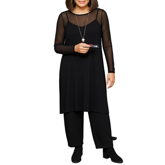 Woman in a black outfit standing in a room with a table and bookshelf.