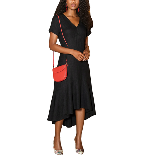 Woman in a black dress with a red handbag standing in an outdoor evening setting with tables and decorations.