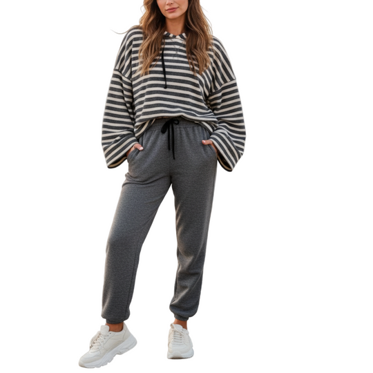 Woman wearing a striped sweater and gray sweatpants standing on a beach.