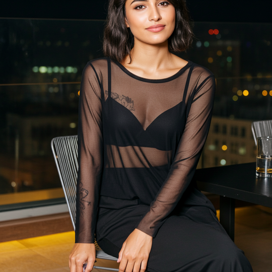 Woman wearing a sheer black dress sitting at a table with a blurred cityscape background