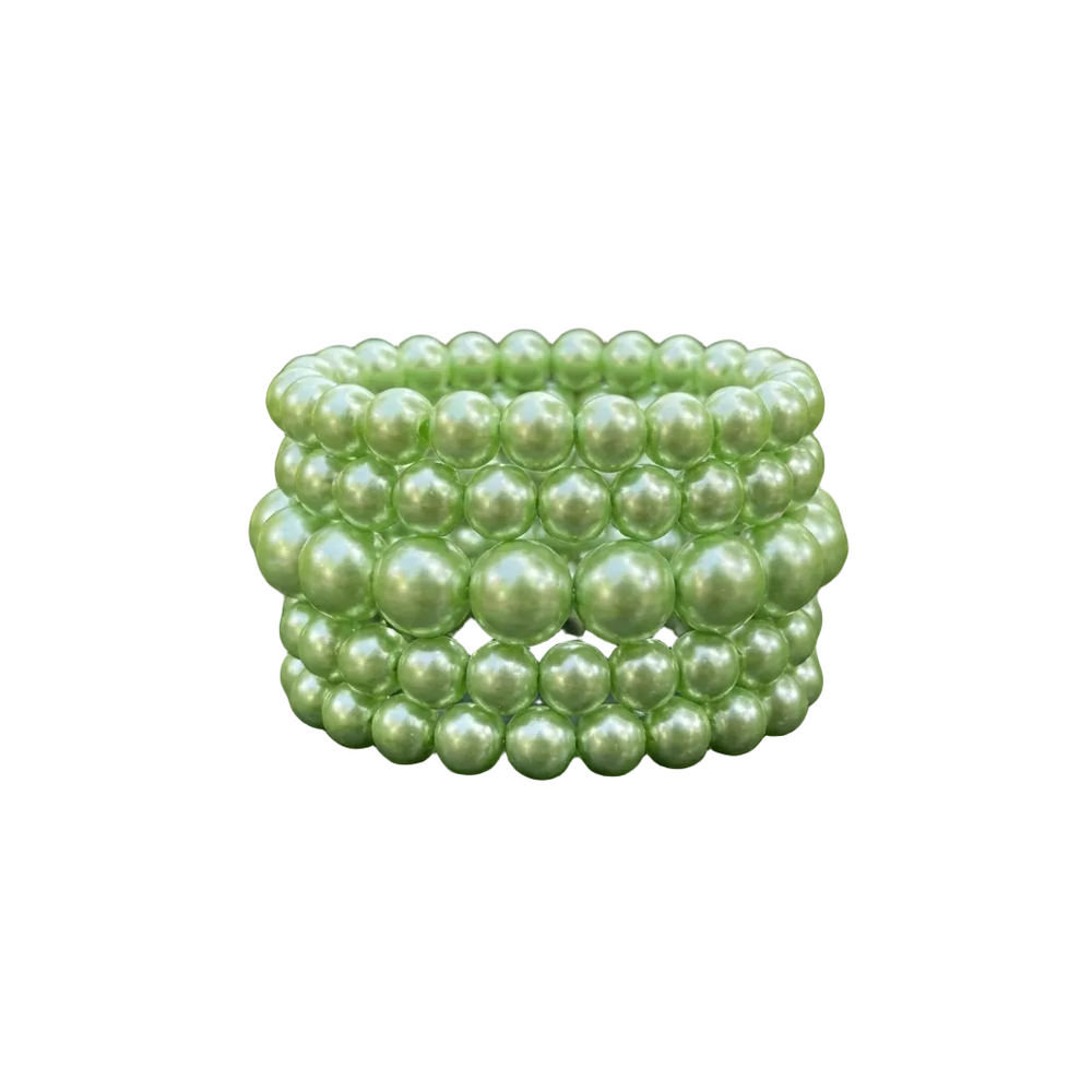 Stack of green pearl bracelets on a dark surface with green leaves in the background