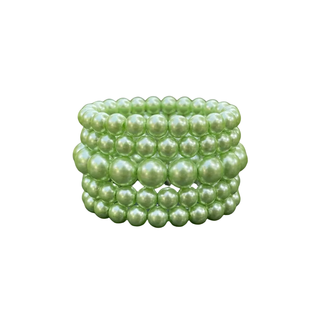 Stack of green pearl bracelets on a dark surface with green leaves in the background