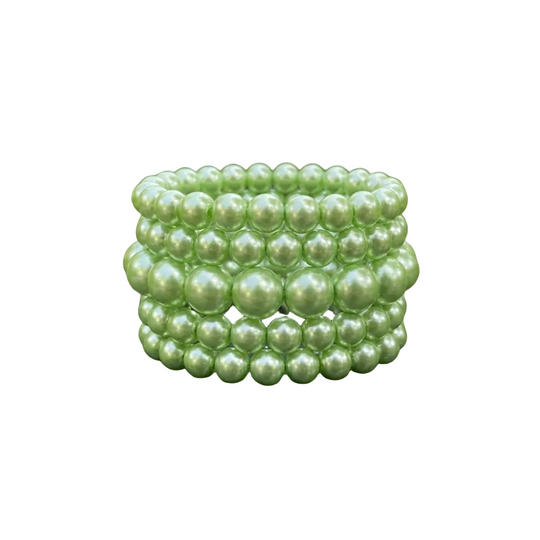 Stack of green pearl bracelets on a dark surface with green leaves in the background