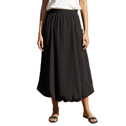 Person wearing a black skirt standing outdoors with plants in the background