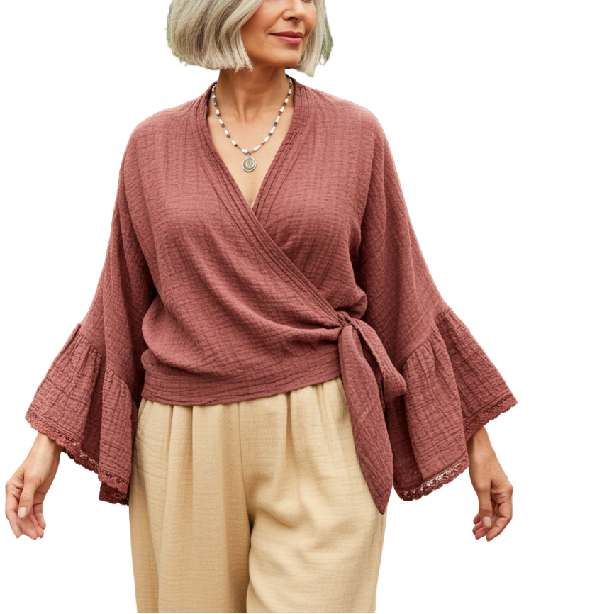 Woman in a pink top and beige pants standing in a greenhouse with plants around.