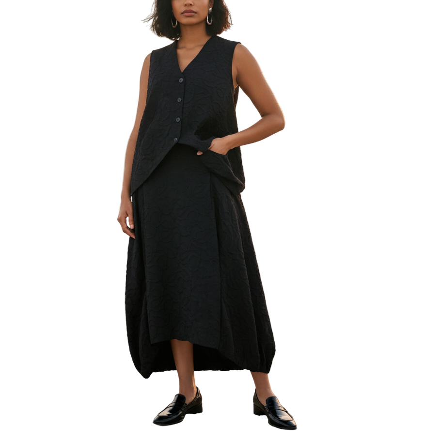 Woman in a black sleeveless dress standing on a beach at sunset