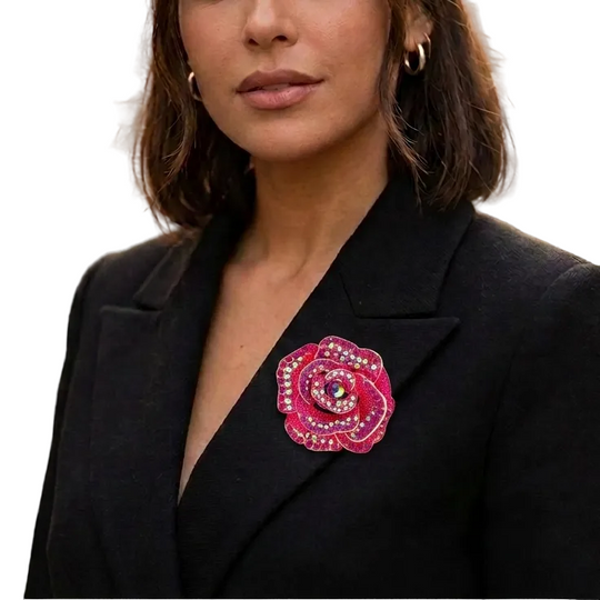 A woman wearing a black blazer and gold hoop earrings, featuring a prominent pink rose brooch embellished with rhinestones on her left lapel, set against a blurred city street background.