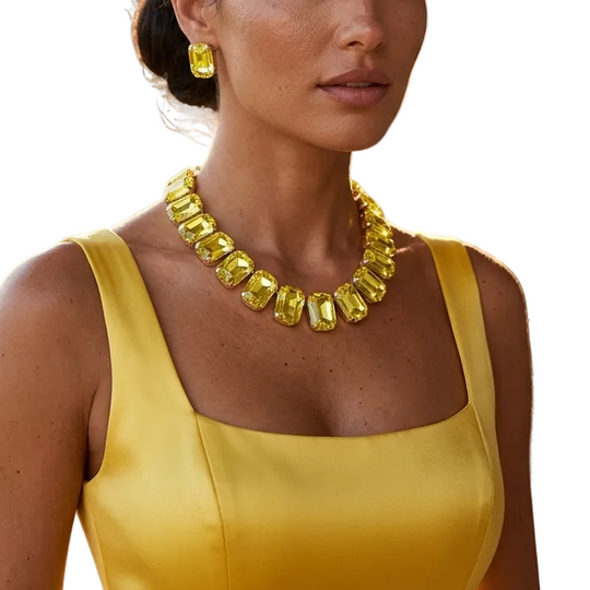 A woman wearing a bright yellow gemstone necklace and matching yellow earrings, styled with a yellow satin dress, set against a warm, sunlit outdoor background with stone columns and greenery.