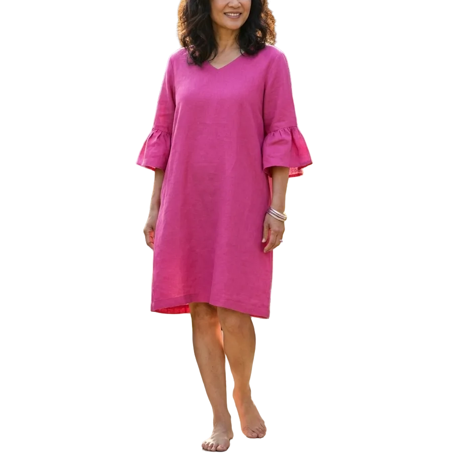 Woman in a pink dress standing in a garden with potted plants and a table with a pitcher of iced tea.