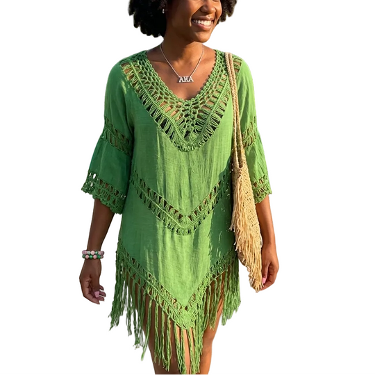 Woman in a green dress with fringe standing by a poolside with palm trees in the background