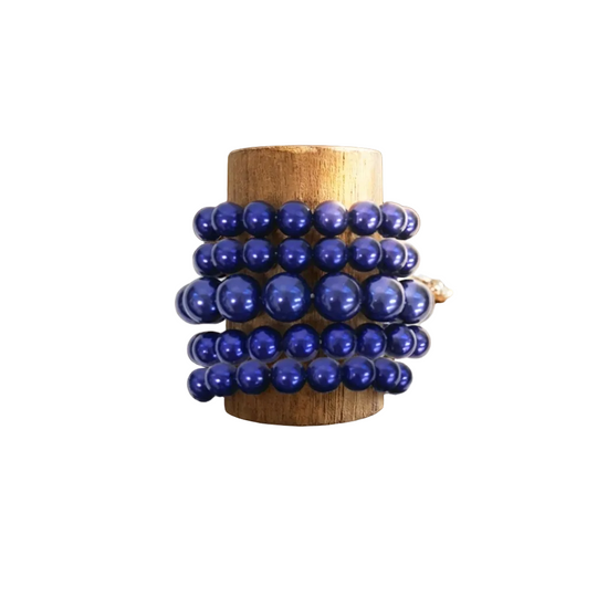 Stack of blue beaded bracelets on a wooden stand with jewelry on a rustic wooden surface.