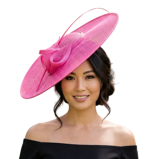 Woman wearing a large pink hat with a blurred outdoor background