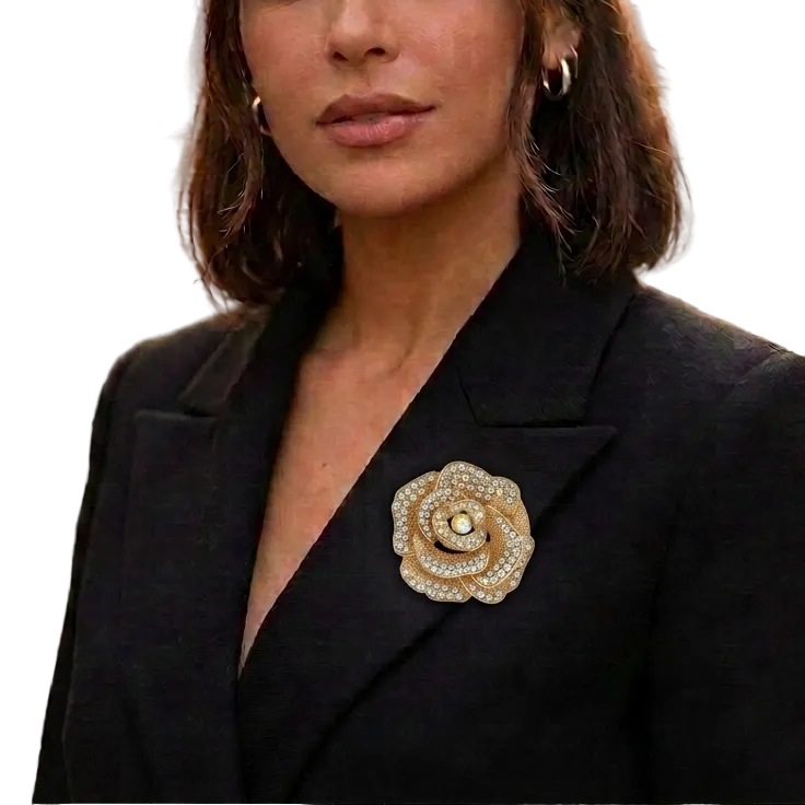 A woman wearing a black blazer and small hoop earrings, featuring a prominent gold rose-shaped brooch embellished with rhinestones on her left lapel, set against a blurred city street background.