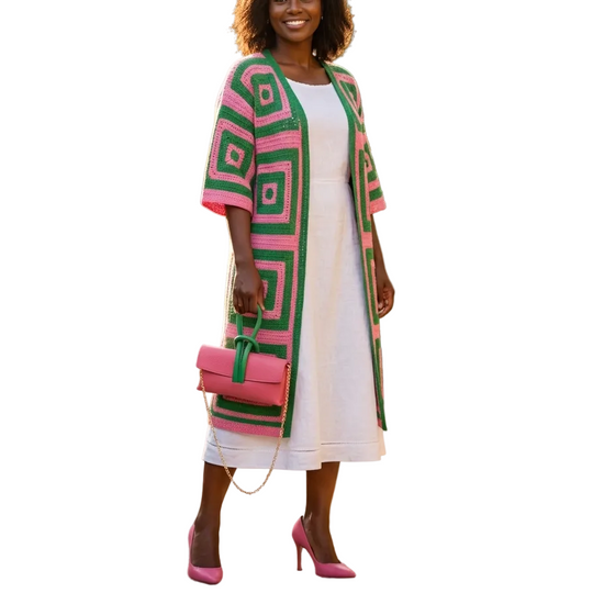 Woman in a white dress with a green and pink patterned cardigan standing in a garden.