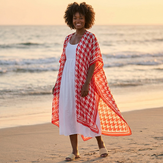 Woman on a beach wearing a red and white patterned cover-up over a white dress.