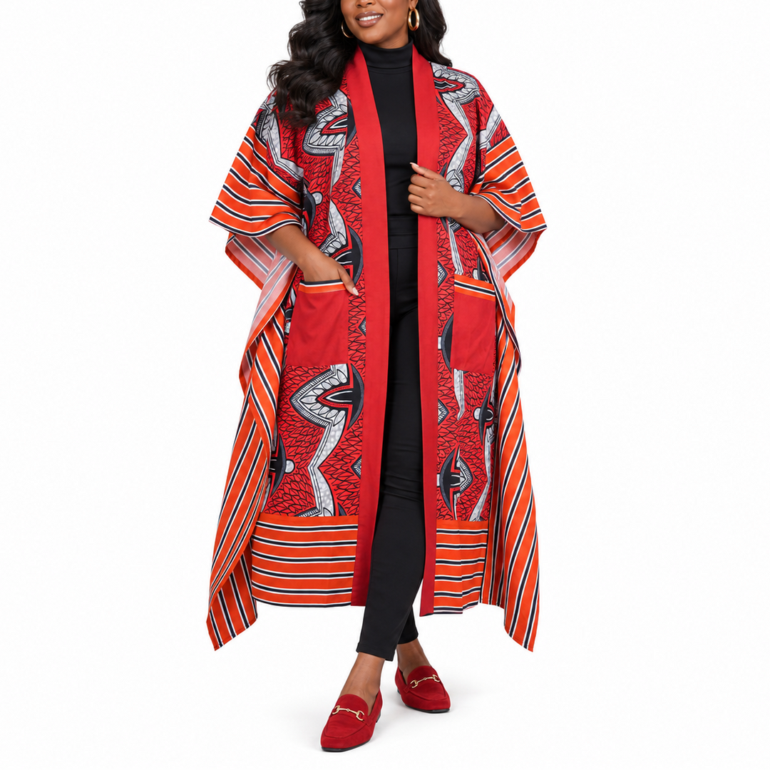 A woman modeling a long red open-front cardigan with a bold black, white, and orange African wax print pattern, styled over a black outfit and red loafers against a plain white background.