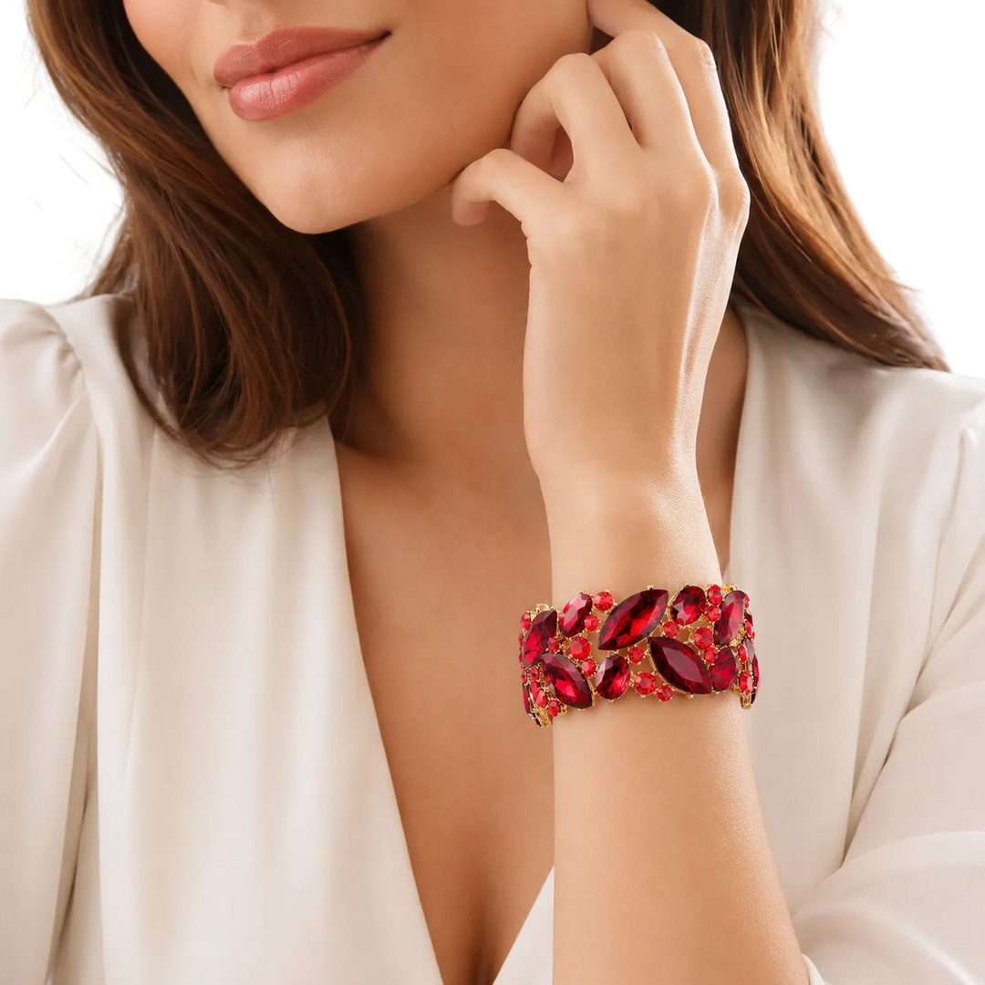 A close-up of a woman wearing a wide red crystal bracelet with gold-toned detailing, paired with a cream-colored blouse.