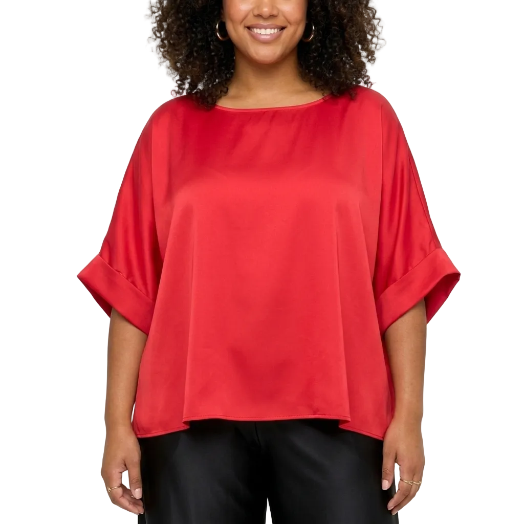 A woman wearing a bright red, short-sleeved top with rolled cuffs and black pants, standing against a light gray background.