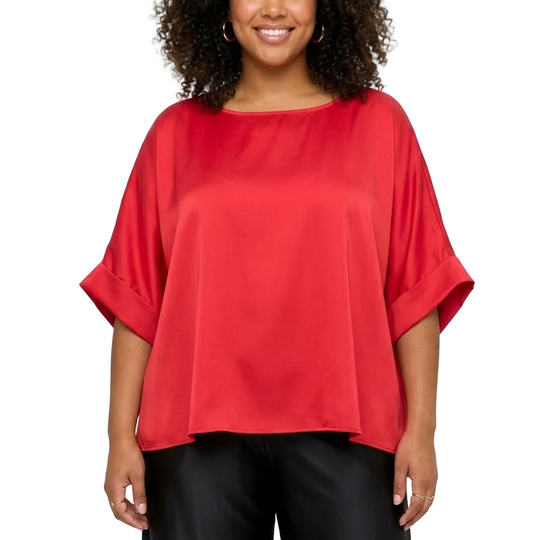 A woman wearing a bright red, short-sleeved top with rolled cuffs and black pants, standing against a light gray background.