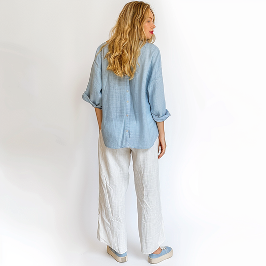 Woman wearing a light blue shirt and white pants on a plain background