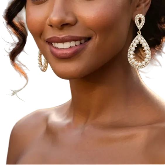 A smiling woman with styled dark curly hair wears large teardrop-shaped dangling earrings with a white and gold beaded design, photographed outdoors at night with blurred guests and string lights in the background.