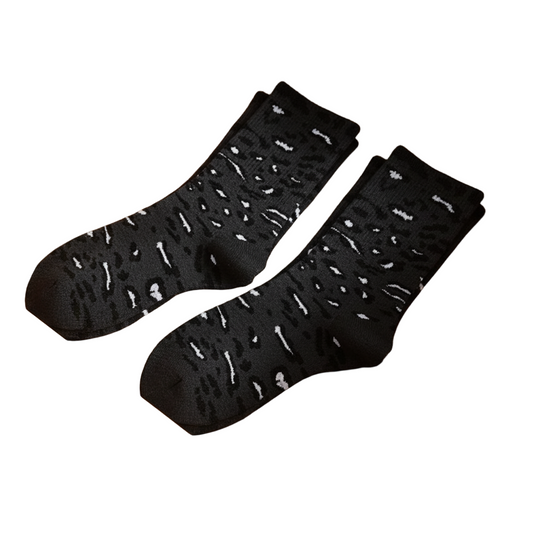Black patterned socks in a wooden drawer with other pairs in the background.