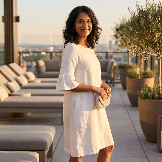 Woman in a white dress standing on a rooftop terrace with lounge chairs and plants.
