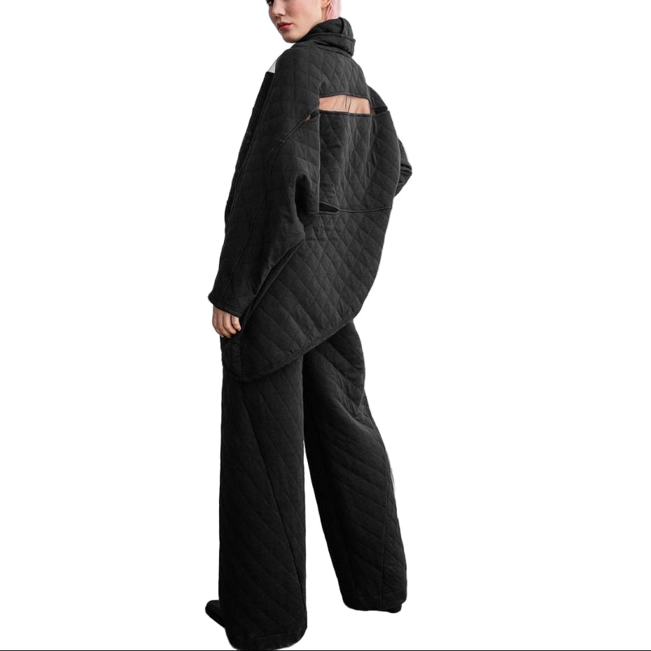 Person wearing a dark gray outfit standing in a minimalistic room with a framed picture on the wall.